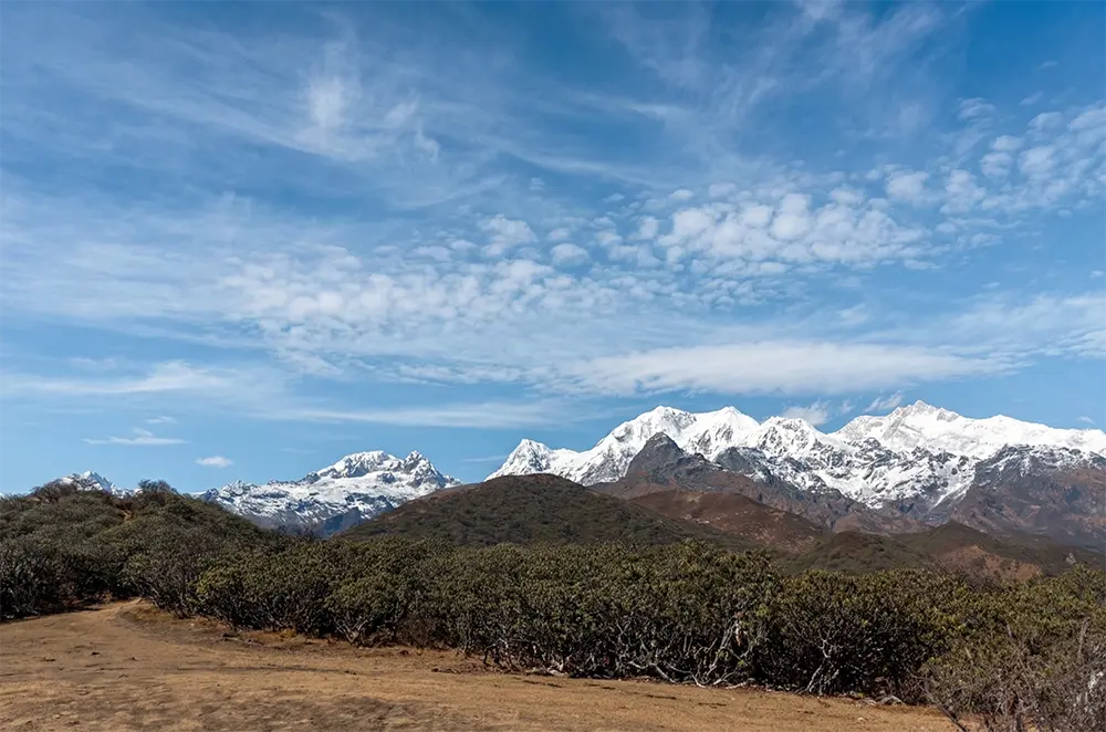 Panoramic Himalayan mountain view along the Dzongri Trek trail in West Sikkim under a clear blue sky.