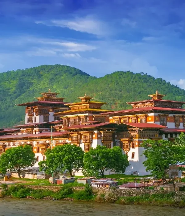 Punakha Dzong monastery in Bhutan with traditional Bhutanese architecture beside a river and lush green hills under blue sky